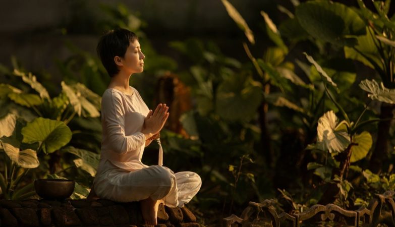 Serene scene of a woman meditating in a lush garden setting at daylight.