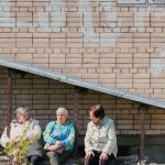 Elderly women sit outside beneath a brick wall.