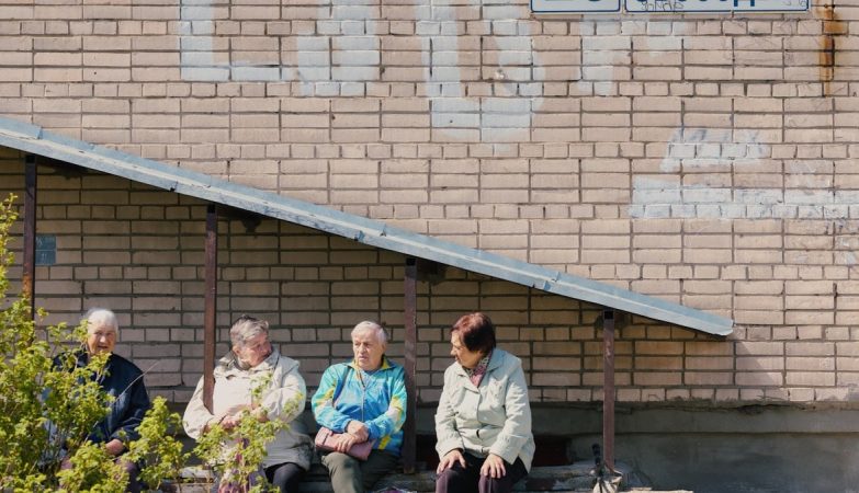 Elderly women sit outside beneath a brick wall.